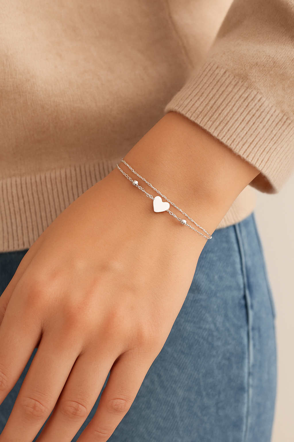 Silver bracelet with a heart charm on a wrist against a neutral background