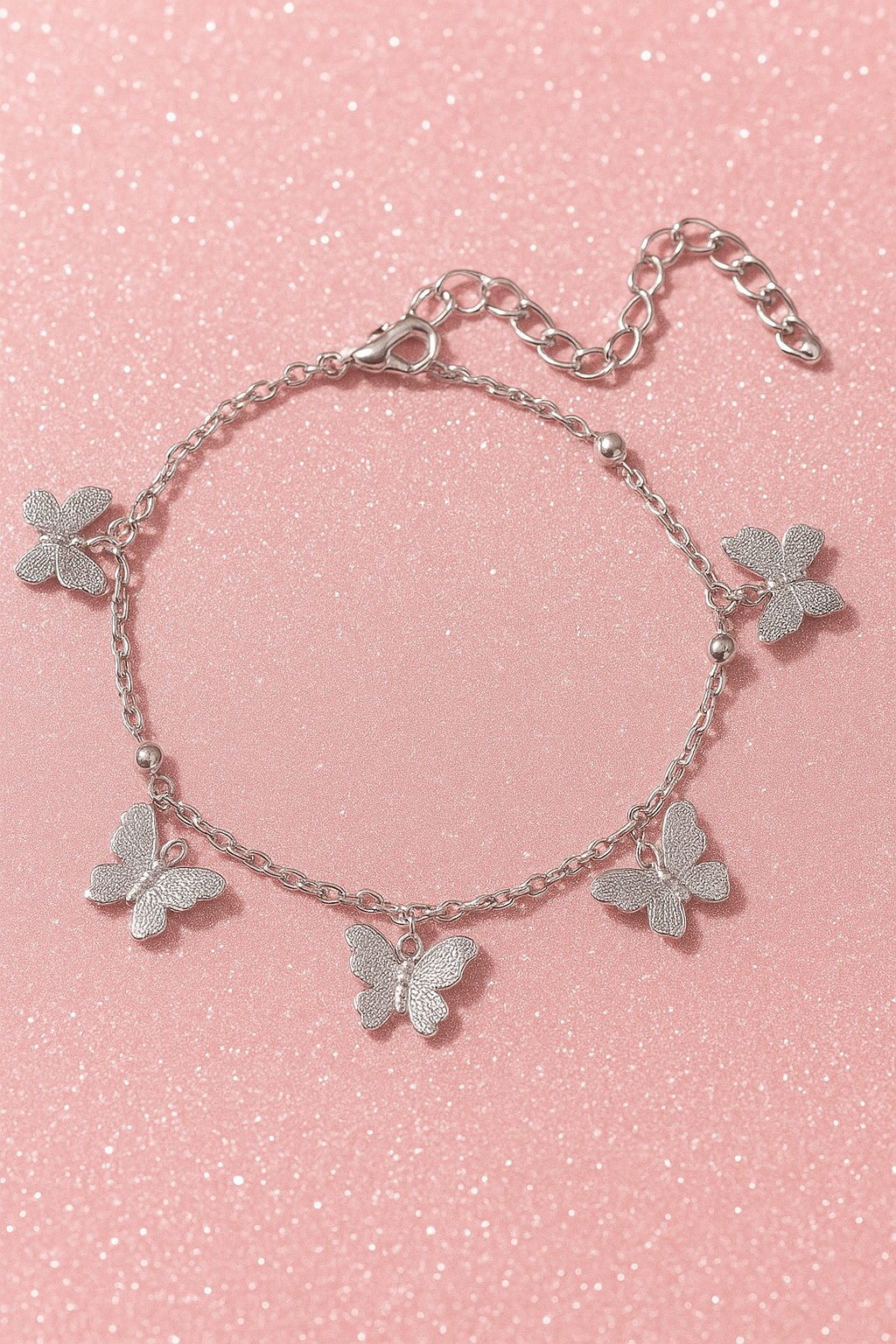 Silver butterfly charm bracelet on a pink glitter background